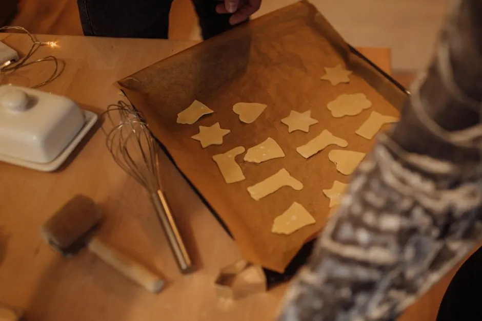 Freshly cut cookie dough in various shapes on baking tray with whisk nearby.